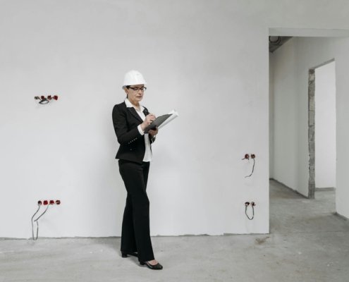 Woman in hard hat reviews notes at a construction site, examining progress.